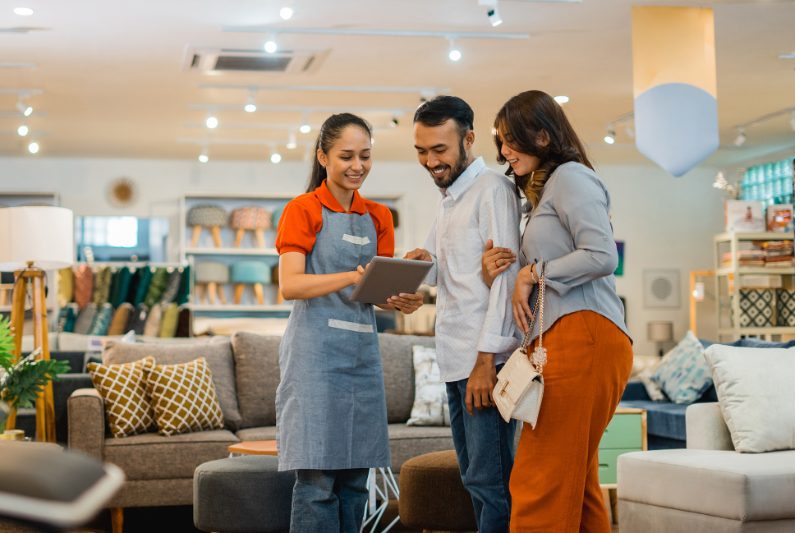 female shop assistant serving a husband and wife customer with a tablet at a furniture store