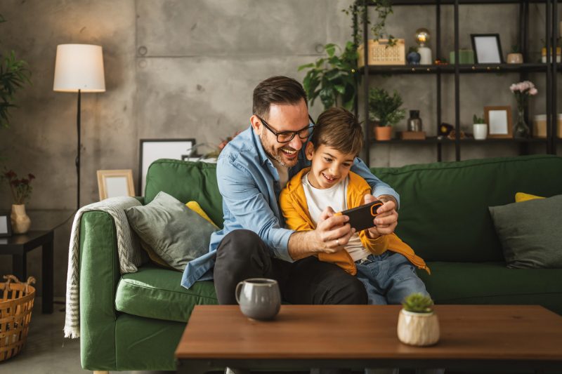 Father and son play video games on a mobile phone and enjoy at home